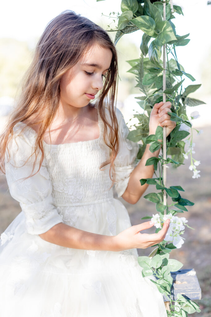 Little girl fairy garden swing birthday portraits in white dress