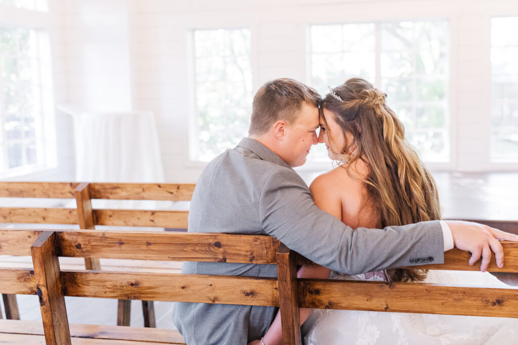 Intimate portrait of bride and groom sitting on a pew in a white chapel by cecilly elaine photography